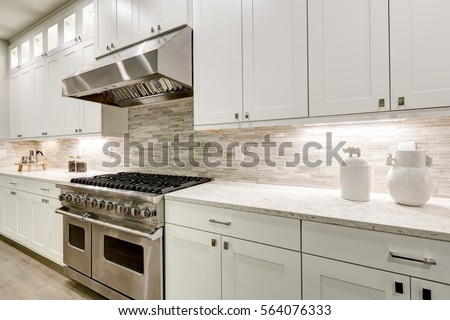 Gourmet kitchen features white shaker cabinets with marble countertops paired with stone subway tile backsplash and stainless steel hood over eight burner gas range. Northwest, USA