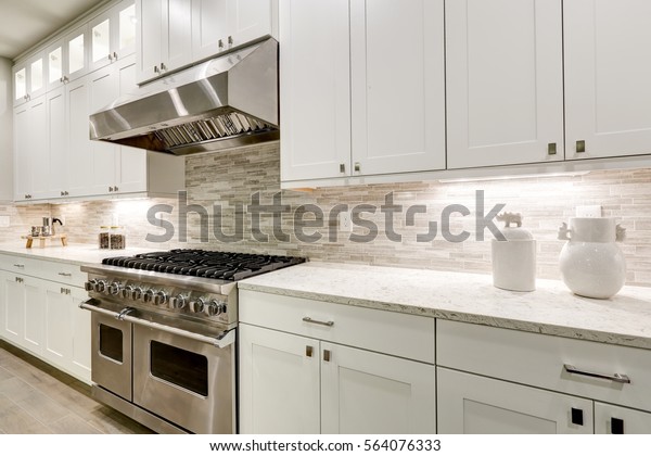 Gourmet\
kitchen features white shaker cabinets with marble countertops\
paired with stone subway tile backsplash and stainless steel hood\
over eight burner gas range. Northwest,\
USA