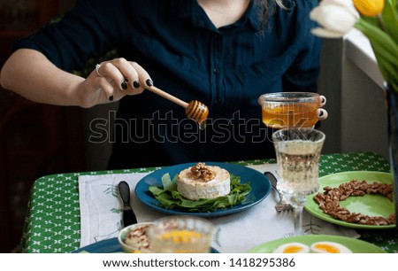 A gourmet lunch for two: grilled camembert with spinach, boiled eggs, a bowl with honey and walnuts and two glasses of wine; a vase with tulips on a green tablecloth.