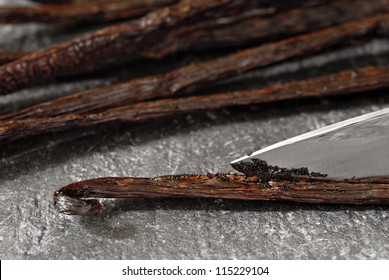 Gourmet Madagascar vanilla beans being split open with a knife to expose the tiny flavor filled seeds.  Pods are resting on a slate cutting board.  Macro with shallow dof.