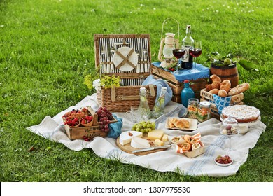 Gourmet picnic spread with fresh fruit, cheese, wraps, crusty bread, wine and dessert surrounding a wicker hamper on green grass in a park - Powered by Shutterstock