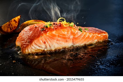 Gourmet portion of thick juicy fresh salmon grilling on a griddle seasoned with lemon zest, herbs and spices in a low angle view with copyspace and rising steam