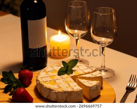 A gourmet romantic dinner table features a bottle of wine, two empty wine glasses, a wheel of Brie cheese drizzled with honey, fresh strawberries, and candlelight.