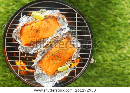 Gourmet salmon steaks grilling on a barbecue in tin foil wrappers garnished with leomon wedges, overhead view