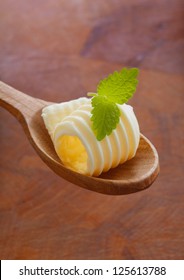 Gourmet Shaving Or Curl Of Rolled Butter Or Margarine Garnished With Fresh Mint Being Offered On A Wooden Salad Spoon Against A Wood Background