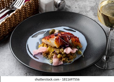 Gourmet Special In A Fancy Restaurant: Fried Cod Fillet With Couscous And Blue Sauce On A Wide Black Plate