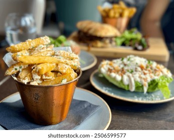 Gourmet truffle fries served in a copper cup alongside a wedge salad and a burger on a rustic table in a casual dining restaurant setting. Other table food blurred in background for a full meal. - Powered by Shutterstock