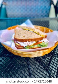 Gourmet Turkey Sandwich On Rye Whole Wheat Bread With Deli Meat Lettuce Tomato Avocado In Food Basket Healthy Eating On Table Outside
