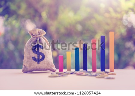 Government budget / public spending concept : Dollar bag, coins, color wood bar graph on a table, depicts the increment in annual financial budget or revenues that government collects from tax payer.