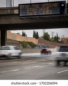 Government Digital Freeeway Sign At Overpass With Message Stating “Stop The Spread ,Stay Home, Save Lives” And Traffic Blurred Under The Sign During The Coronavirus Pandemic  