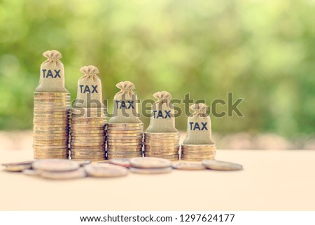 Government income tax collection concept : Tax burlap bags on rows of rising coins, depicts the levying of taxes that aims to raise revenue to fund governing or alter prices in order to affect demand