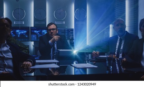 Government Officials, Military Men And Top Corporate Executives Watching Presentation In The Conference Room. Working Projector On The Table.