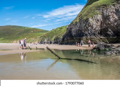 Gower Peninsula, UK - 7 August 2020:  Scenic view of people exploring the ship wrecks, pools and cliffs of Rhossili Bay beach, on the Gower Peninsula near Swansea, Wales.
