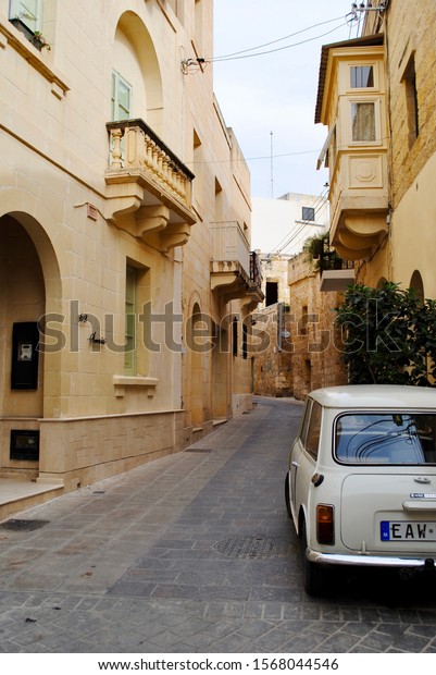 Gozo, Malta\
- 2014: A narrow alley with just enough room for a vintage, cream\
Innocenti Mini 1000 with Maltese European narrow license plates.\
Homes with typical Maltese\
balconies.