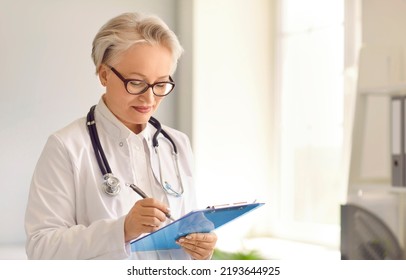 GP Doctor With Clipboard. Middle Aged Mature Woman In White Lab Coat And Glasses Writing Checklist Or General Examination Result, Filling In Medical Document Or Prescribing Treatment. Medicine