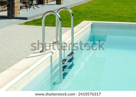 Grab bars ladder in the blue swimming pool. Ladder stainless handrails for descent into swimming pool. Vacation concept