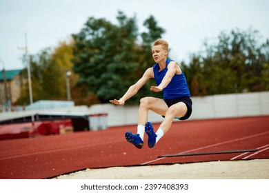 Graceful arch as a runner jumps into sand. Dynamic portrait of athletic man, professional sportsman doing perfect long jump. Concept of kinds of sport, championship, motivation, energy. - Powered by Shutterstock