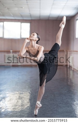 Graceful Asian ballerina in a beige bodysuit and black skirt is rehearsing in a dance class. 