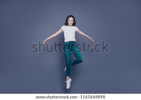 Graceful attractive adorable pretty stylish trendy nice lovely cheerful curly-haired brunette girl in casual white t-shirt and jeans, raising up in air, isolated on grey background