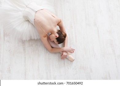 Graceful ballerina in pointe shoes at white wooden floor makes ballet leg stretching. Ballet practice of classical dancer, copy space - Powered by Shutterstock