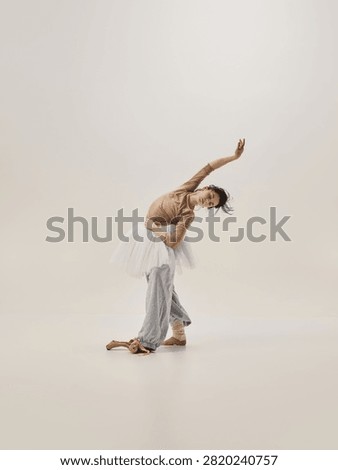 Graceful ballerina practicing deep side bend in tutu and warmup pants on minimalist studio background. Concept of dance flexibility, warmup routine, body awareness.