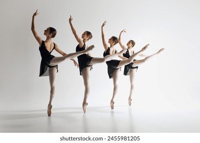 Graceful ballet performance. Four graceful ballet dancers, teens in black leotards and pointe standing in md-pose, practicing against grey studio background. Concept of ballet art, dance studio, youth - Powered by Shutterstock