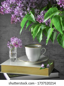 A graceful cup of coffee on a stack of books next to a bouquet of lilacs. Tender still life of a happy morning of romantic nature. Spring