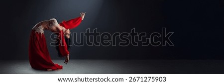 A graceful dancer in a red outfit performs a delicate pose on a dark backdrop, offering elegant movement with copy space. Ideal for ads and artistic projects.