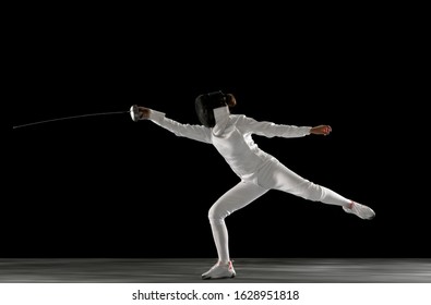 Graceful. Teen Girl In Fencing Costume With Sword In Hand Isolated On Black Background. Young Female Model Practicing And Training In Motion, Action. Copyspace. Sport, Youth, Healthy Lifestyle.