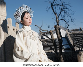 Graceful Woman in Traditional Chinese Attire and Floral Headpiece Posing Outdoors on a Sunny Day with Historic Architecture in the Background. - Powered by Shutterstock