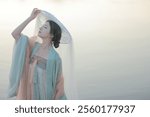 Graceful Woman in Traditional Hanfu with Flowing Veil by a Serene Lakeside at Sunset, Capturing Elegant Asian Cultural Heritage and Tranquility.