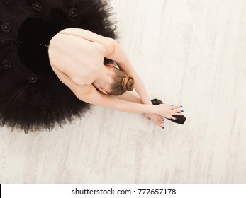 Graceful Young Ballerina In Pointe Shoes At White Wooden Floor Background, Top View From Above With Copy Space. Ballet Practice And Stretching. Back Of Ballet Dancer.