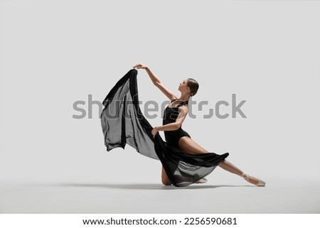 Graceful young ballerina practicing dance moves with black veil on white background