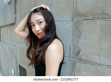 Graceful young woman with long black hair in sundress posing in sunny day. Outdoor photo of cool Chinese girl in trendy summer sexy black dress.