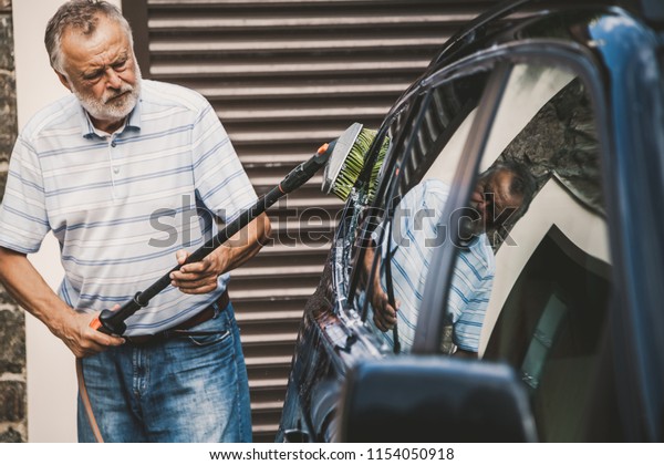 gracious man with a gray beard washes a\
black car with a special brush on a long\
handle\
