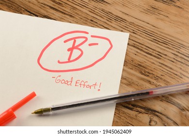 A Graded School Paper Marked In Red Ink Over A Wood Desktop.