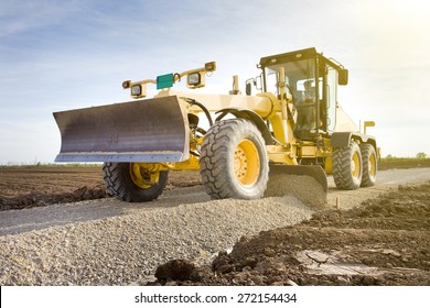 Grader leveling gravel on road construction site