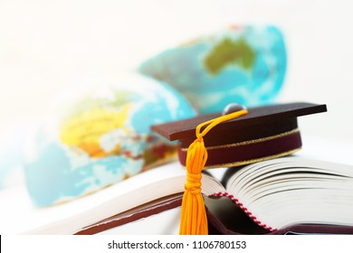 Graduate or Education knowledge learning study abroad concept : Graduation cap on opening textbook with blur of america australia earth world globe model map in Library room of campus, Back to School 