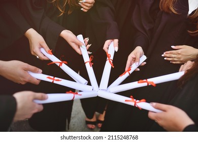 graduate students in black robes holding diplomas or certificates of graduation from a higher educational institution. - Shutterstock ID 2115248768