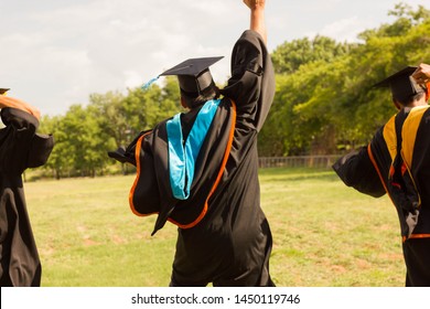 Graduate Students Wear Black Graduation Dresses. Holding The Graduation Certificate Is Showing A Happy Gesture. Jump To Sky