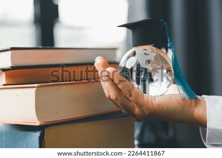 Graduate study abroad program concept : Black graduation cap on a globe map and books, depicts knowledge can be learned online anywhere and everywhere, even in universities or campus around the world.