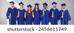 Graduate.Banner with group portrait of happy joyful smiling mixed race multiethnic university students with diplomas in blue graduation caps and gowns standing together on light grey wall background