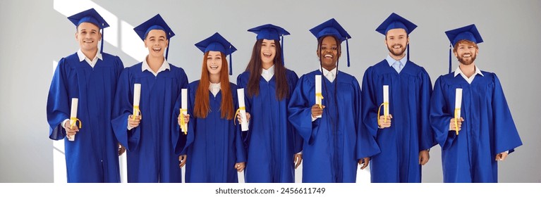 Graduate.Banner with group portrait of happy joyful smiling mixed race multiethnic university students with diplomas in blue graduation caps and gowns standing together on light grey wall background - Powered by Shutterstock