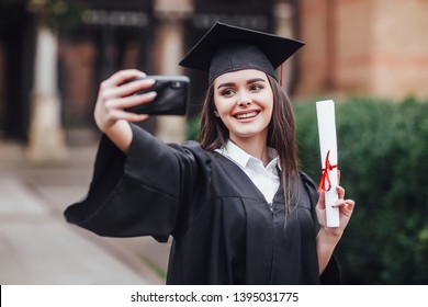 Graduated Woman In Graduation Hat And Gown , Outdoors Make Joint Selfie!