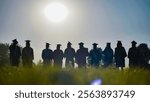 Graduates in cap and gown stand in a field at sunset, commemorating their high school graduation