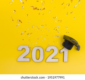 Graduation 2021 wooden number 2021 in a graduate hat with confetti on a yellow background top view. Square photo