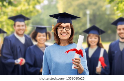 Graduation, Adult Education And Old People Concept - Happy Senior Graduate Student Woman In Mortar Board With Diploma Laughing Over Group Of Classmates In Summer Park Background