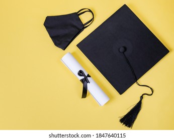 
Graduation cap, diploma and black cotton mask on the right on a yellow background with space for text on the left, top view close-up.