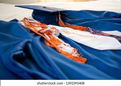 Graduation cap and gown with honors sash laid across a white bed in bright morning day light. Feng Shui accomplishments image for awards - Shutterstock ID 1392395408