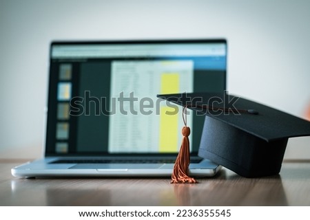Graduation cap with laptop pace on wood table background.